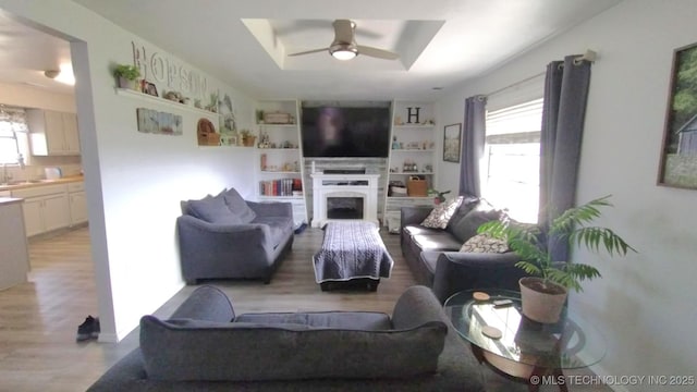 living room with a raised ceiling, a healthy amount of sunlight, a fireplace, and a ceiling fan