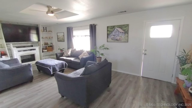 living area featuring visible vents, a fireplace, a ceiling fan, and wood finished floors