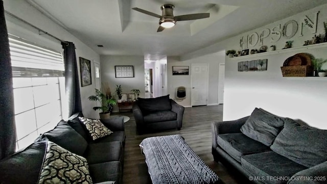 living area with wood finished floors, a raised ceiling, and ceiling fan