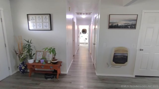 hall featuring heating unit, wood finished floors, visible vents, and baseboards