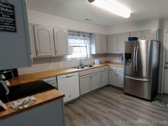 kitchen with white dishwasher, a sink, stainless steel refrigerator with ice dispenser, wood counters, and backsplash