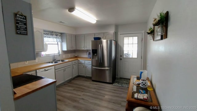 kitchen featuring a sink, wood finished floors, white dishwasher, butcher block counters, and stainless steel fridge with ice dispenser