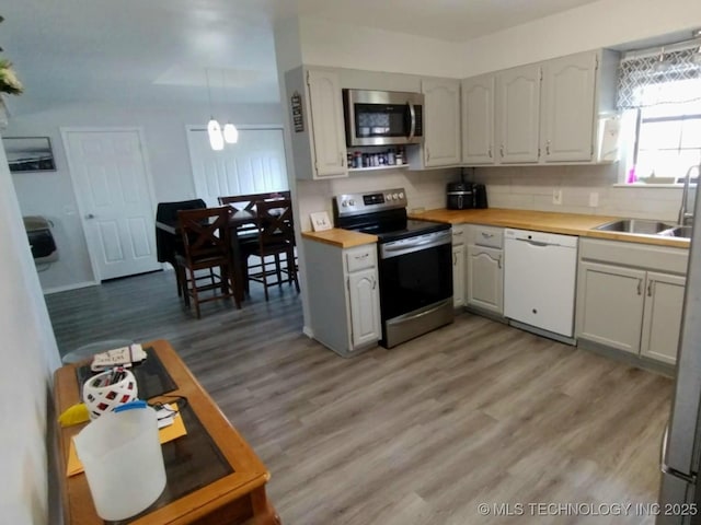 kitchen with a sink, stainless steel appliances, tasteful backsplash, and light wood finished floors