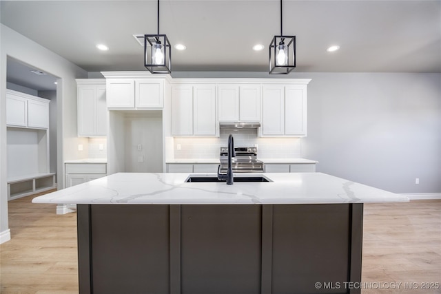 kitchen featuring light wood finished floors, light stone countertops, under cabinet range hood, white cabinets, and a sink