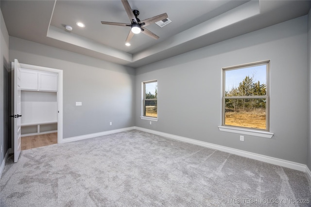 unfurnished bedroom with baseboards, carpet floors, recessed lighting, a walk in closet, and a raised ceiling