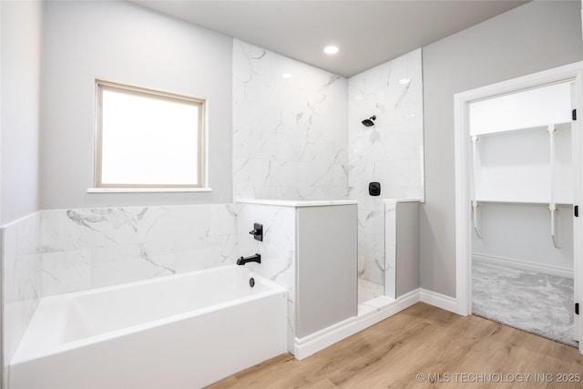 full bath featuring wood finished floors, a marble finish shower, recessed lighting, a spacious closet, and a garden tub