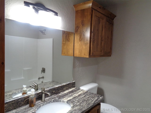 full bath featuring shower / bathing tub combination, toilet, vanity, and a textured wall