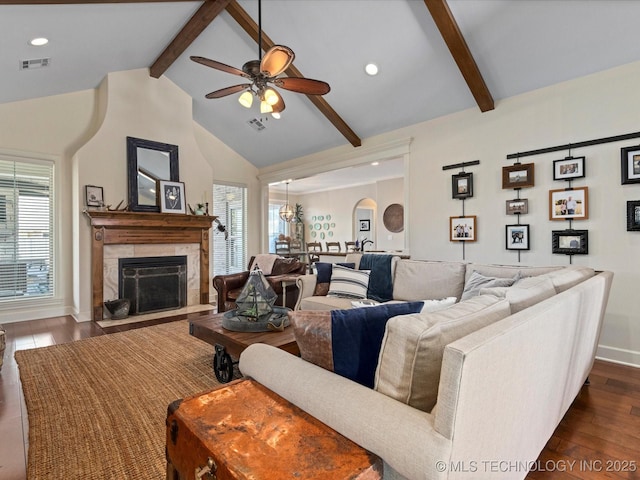 living area with visible vents, dark wood finished floors, ceiling fan, a tile fireplace, and beamed ceiling