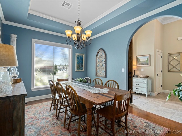 dining area with visible vents, ornamental molding, arched walkways, an inviting chandelier, and a raised ceiling