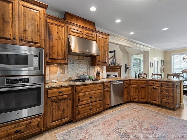 kitchen with light stone countertops, stainless steel appliances, under cabinet range hood, crown molding, and backsplash