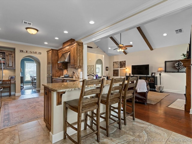 kitchen featuring lofted ceiling with beams, visible vents, arched walkways, and under cabinet range hood