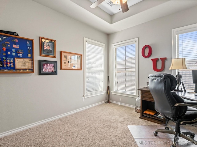 carpeted office space with visible vents, a ceiling fan, a tray ceiling, and baseboards