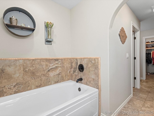 bathroom with baseboards, a bath, and a spacious closet