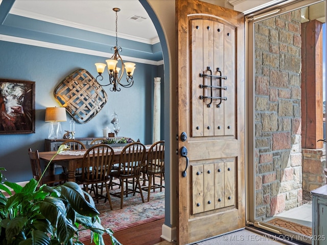 foyer entrance featuring a chandelier, arched walkways, visible vents, and ornamental molding