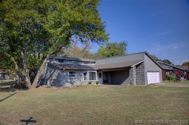 view of front of property featuring a garage, driveway, a front yard, and stone siding