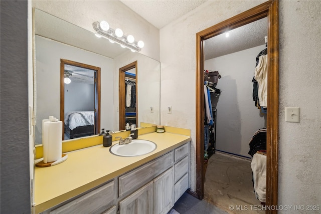 ensuite bathroom featuring a walk in closet, vanity, ensuite bath, a textured ceiling, and a ceiling fan