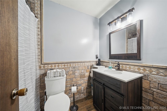 bathroom with a wainscoted wall, toilet, tile walls, and vanity