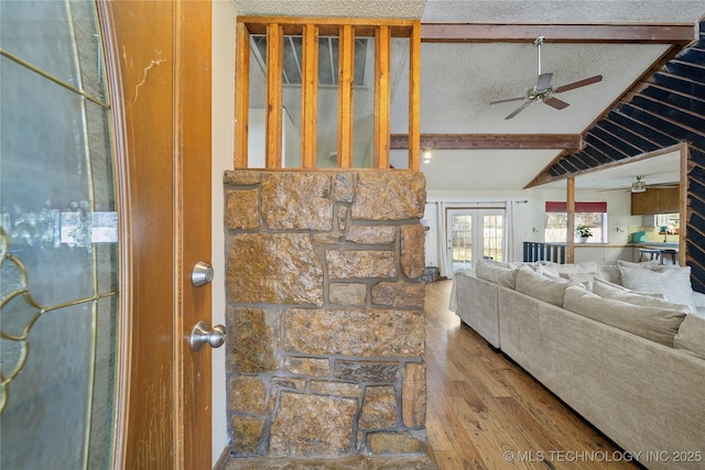 living room with a ceiling fan, a textured ceiling, wood finished floors, french doors, and vaulted ceiling with beams