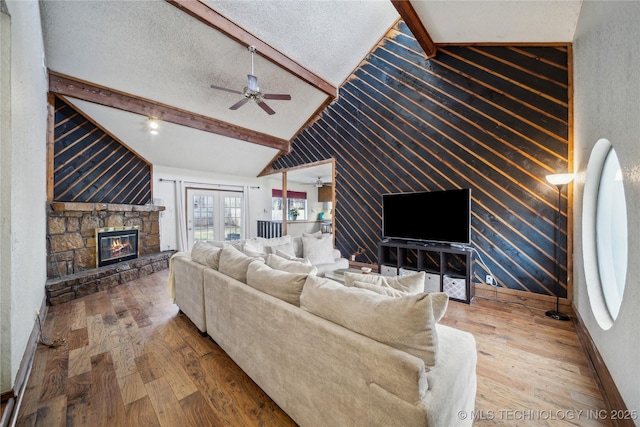 living area featuring lofted ceiling with beams, a fireplace, a textured ceiling, a ceiling fan, and wood-type flooring