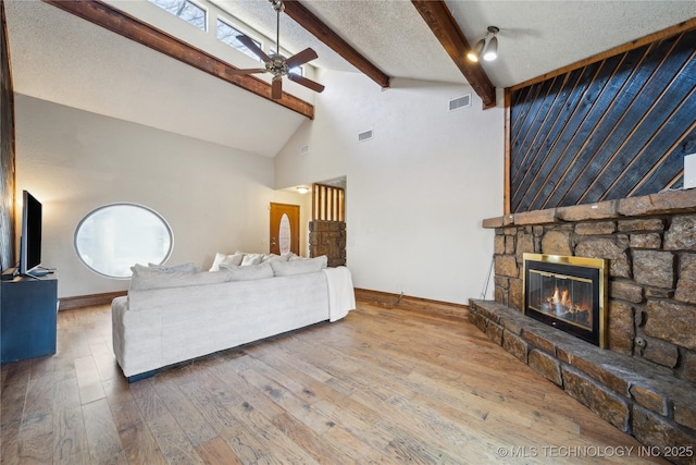 living room featuring hardwood / wood-style floors, visible vents, ceiling fan, a textured ceiling, and beamed ceiling