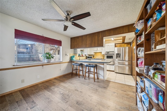 kitchen with light wood-style flooring, a peninsula, a ceiling fan, and stainless steel fridge with ice dispenser