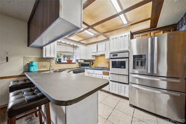 kitchen with a sink, appliances with stainless steel finishes, a peninsula, white cabinets, and light tile patterned floors