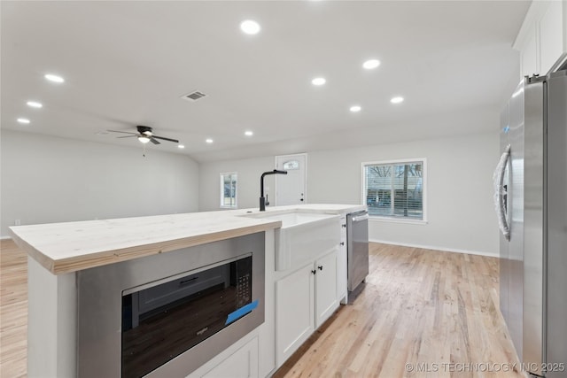 kitchen featuring appliances with stainless steel finishes, white cabinetry, light wood-style floors, and a sink