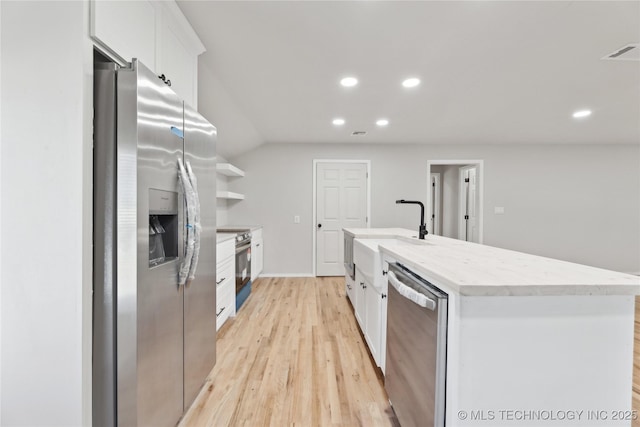 kitchen with visible vents, an island with sink, a sink, stainless steel appliances, and white cabinets