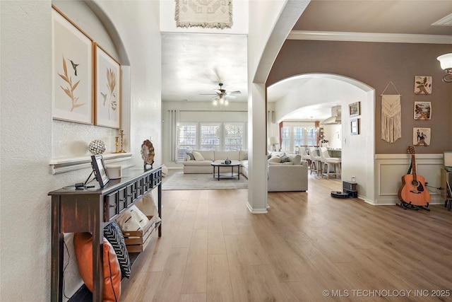 entryway with arched walkways, light wood finished floors, ceiling fan, and ornamental molding