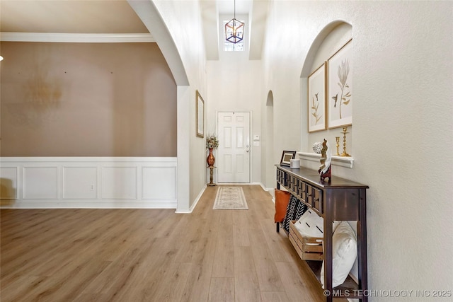 foyer entrance featuring a wainscoted wall, light wood-style flooring, arched walkways, crown molding, and a decorative wall