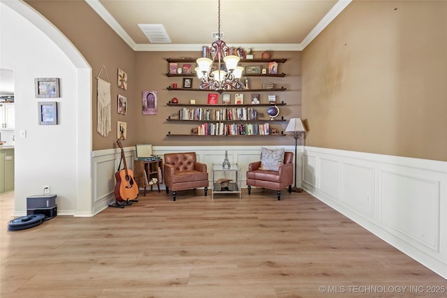 sitting room featuring arched walkways, an inviting chandelier, ornamental molding, and light wood finished floors