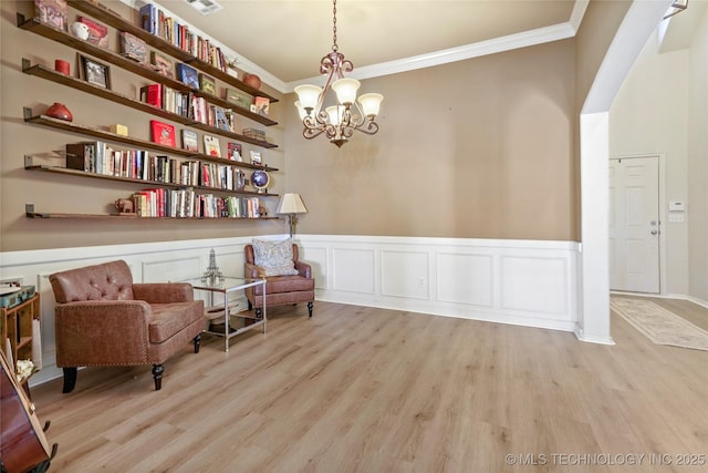 living area featuring light wood-type flooring, a wainscoted wall, a chandelier, and ornamental molding