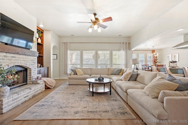 living room with arched walkways, a fireplace, wood finished floors, and a ceiling fan