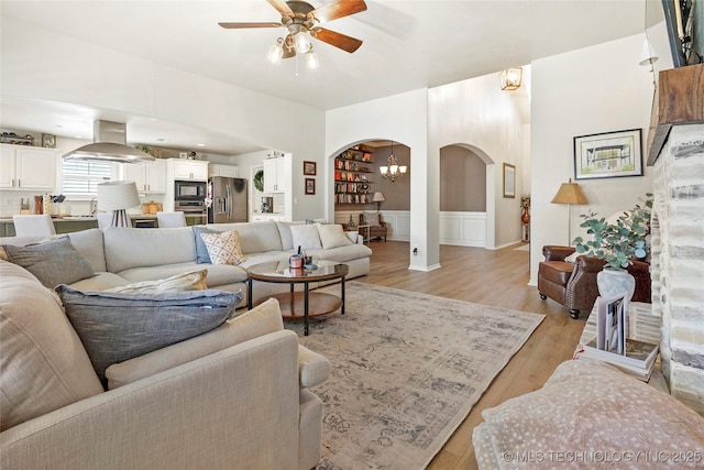 living room featuring light wood-style flooring, arched walkways, and ceiling fan