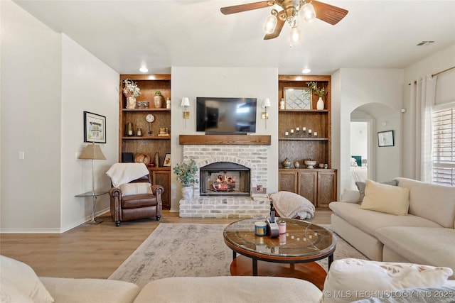 living area featuring visible vents, built in shelves, ceiling fan, wood finished floors, and arched walkways