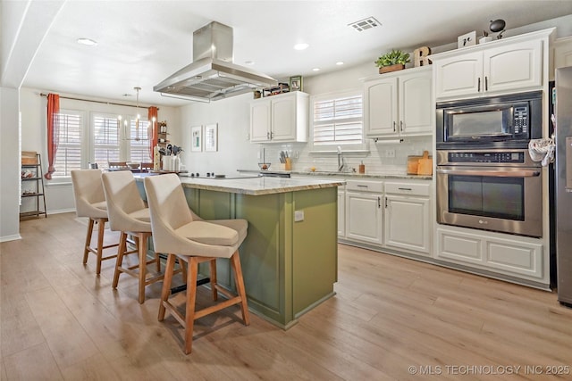 kitchen with visible vents, island exhaust hood, decorative backsplash, black appliances, and a center island