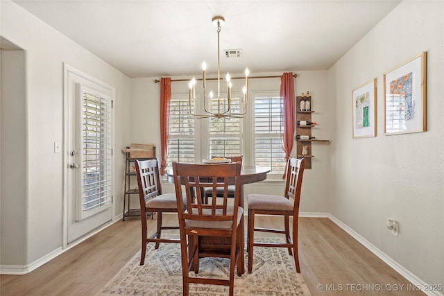 dining room with light wood finished floors, a notable chandelier, baseboards, and visible vents