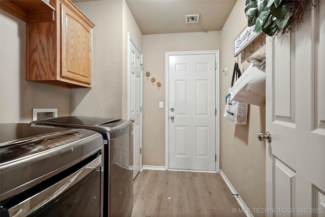 washroom featuring baseboards, visible vents, light wood finished floors, cabinet space, and washer and clothes dryer