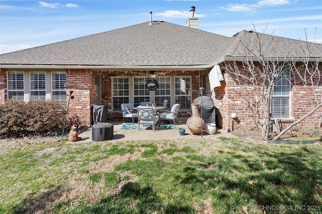 back of property with a shingled roof, a patio area, brick siding, and a chimney