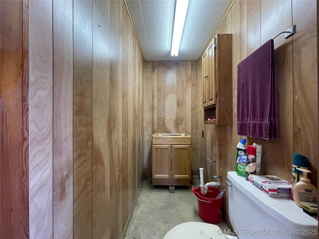 half bathroom with vanity, toilet, concrete flooring, and wood walls