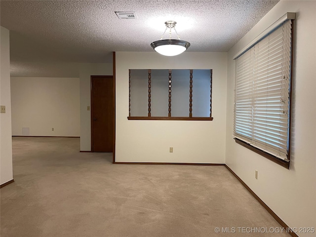 carpeted spare room featuring visible vents, a textured ceiling, and baseboards