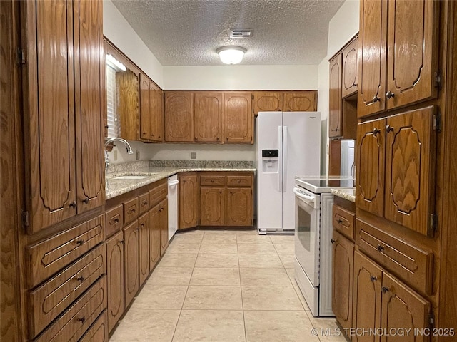 kitchen with visible vents, light tile patterned floors, white appliances, a textured ceiling, and a sink