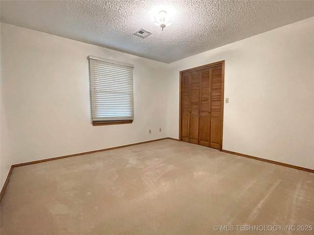 unfurnished bedroom featuring visible vents, light carpet, a textured ceiling, a closet, and baseboards