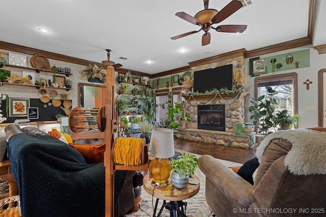 living area featuring a stone fireplace, crown molding, wood finished floors, and ceiling fan