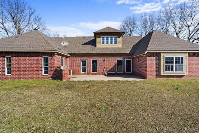 back of property with a shingled roof, a patio area, brick siding, and a lawn