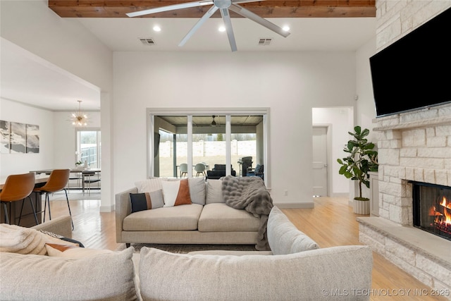 living area with light wood finished floors, visible vents, a stone fireplace, and a ceiling fan