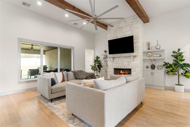 living room featuring a stone fireplace, light wood-style flooring, a ceiling fan, and visible vents