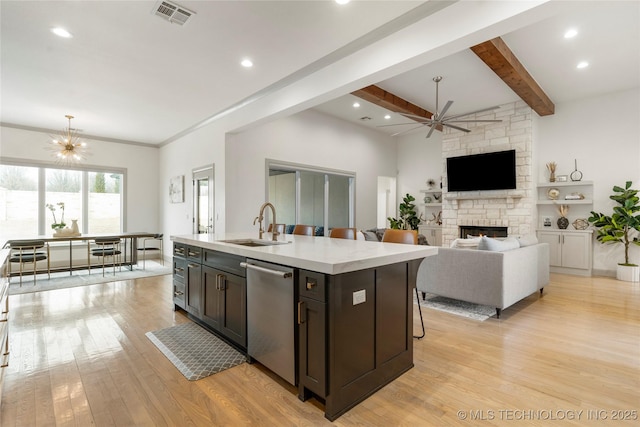 kitchen with visible vents, ceiling fan with notable chandelier, a sink, a stone fireplace, and dishwasher