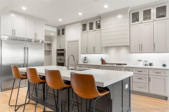 kitchen with tasteful backsplash, a sink, light wood-style flooring, stainless steel appliances, and a kitchen island with sink