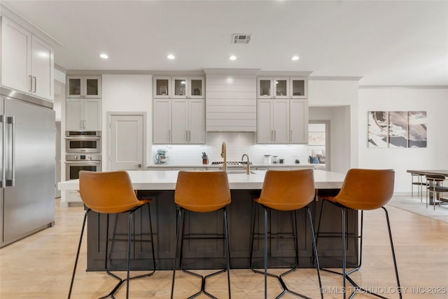 kitchen with visible vents, a kitchen island with sink, tasteful backsplash, stainless steel appliances, and light countertops